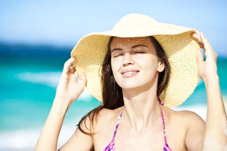 Happy young woman smiling in straw hat with closed eyes on the beach