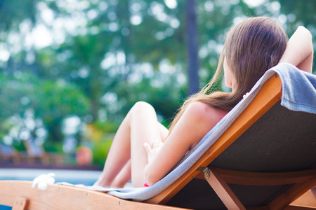 Beautiful young woman with flower in hair relaxing on sun lounger near poolの写真素材