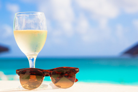 glass of chilled white wine and sunglasses on table near the beachの写真素材