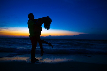 sunset silhouette of young couple in love hugging at beachの写真素材