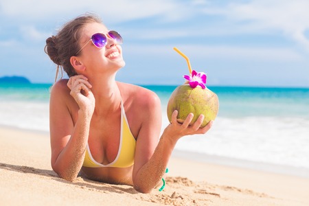 woman in bikini with fresh coconut juice on tropical beachの写真素材