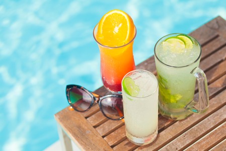 Colorful cocktals and mocktails with tropical pool in background.