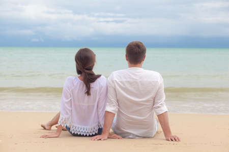 Vacation couple sitting on beach together in love holding around each otherの写真素材
