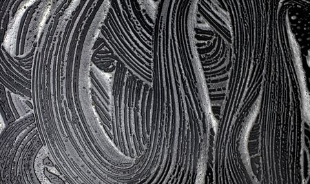 Foamy wave stains on a smooth black surface. Abstract texture background.