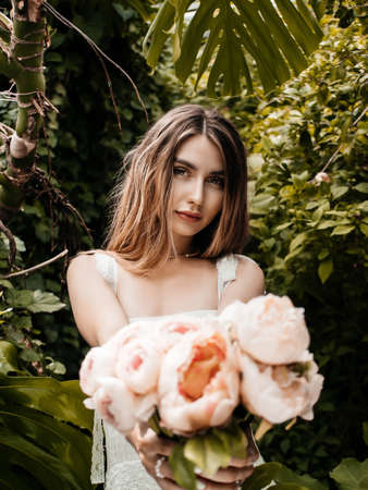 Photo of a girl wearing a dress and holding peonies in a greenhouse. selective focusの写真素材