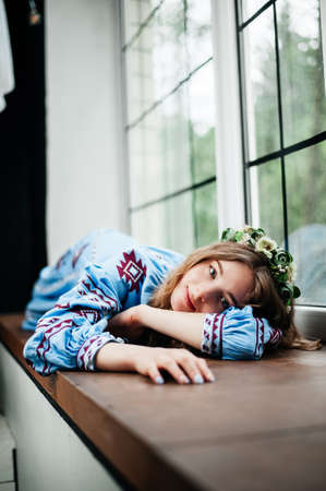 A girl in traditional Ukrainian clothes is lying on the windowsillの写真素材