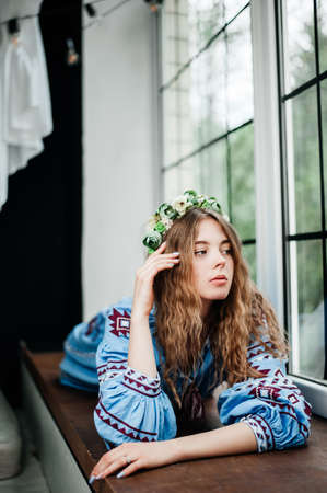A girl in traditional Ukrainian clothes is lying on the windowsillの写真素材