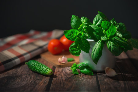 Composition of fresh Basil greens in a metal Cup with other vegetables on a wooden table, in a rustic style. Image with selective focus on Basil leavesの写真素材