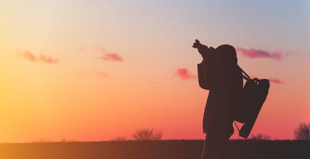 photographer with a tripod and camera takes a landscape during sunset in a large open areaの写真素材