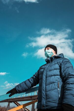 man in blue protective medical mask in the city against the background of the bridge and skyの写真素材