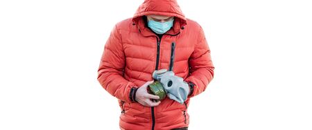 man in a medical mask and a hood holds a gas mask in his hand