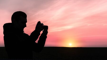 silhouette of a man who takes pictures with an old mechanical camera on a sunset backgroundの写真素材