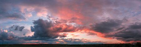sunset panorama with raspberry clouds over a small town against a blue skyの写真素材