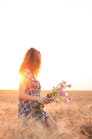 Girl with flowersin hands in a wheat field at sunsetの写真素材
