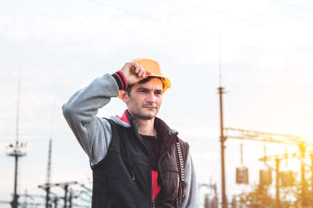 Worker in a helmet against the background of a substation and high-voltage poles