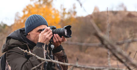 Front view of young male photographer taking pictures in autumn forest