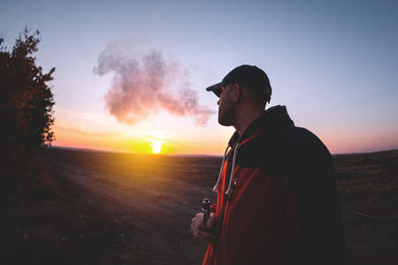 The man smoke an electronic cigarette on the sunset backround