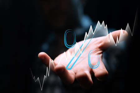 Percent sign and white ascending-bullish chart in the investor's hand on a dark backgroundの写真素材