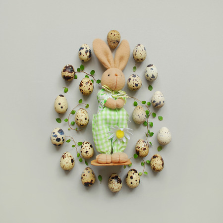 Egg shape made of quail eggs, green leaves and easter bunny rabbit. Minimal Easter concept. Flat lay, top view.の写真素材