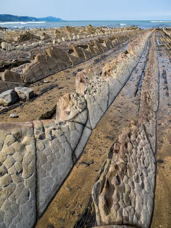 Flysch Coast of Sakoneta, Zumaia, Spain. Flysch is a sequence of sedimentary rock layers that progress from deep-water and turbidity flow deposits to shallow-water shales and sandstones.の写真素材