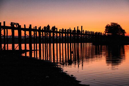 Silhouette of U Bein Bridge at sunrise. It is a crossing that spans Taungthaman Lake, Amarapura in...
