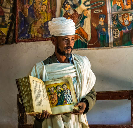 Yeha, Ethiopia - Feb 10, 2020: an orthodox priest shows a painted holy bible from the 14th century...