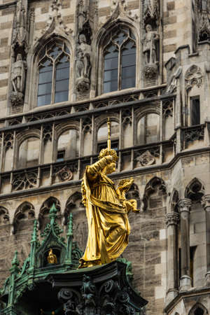 Virgin Mary statue at Marienplatz square, Munich, Germany. This place is a top landmark of Munich. Golden sculpture atop Mariensaule column on background of Town Hall in Munich city center.の写真素材