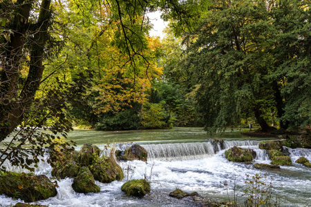 water of the Isar spilling over rocks of green moss and surrounded with tall green trees, in The...
