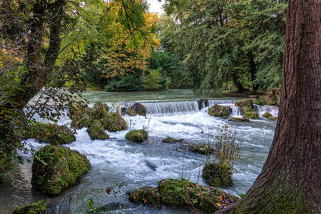 water of the Isar spilling over rocks of green moss and surrounded with tall green trees, in The...
