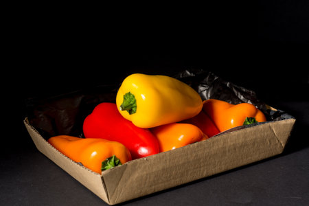 Red, orange and yellow bell peppers in a cardboard box on a black backgroundの写真素材