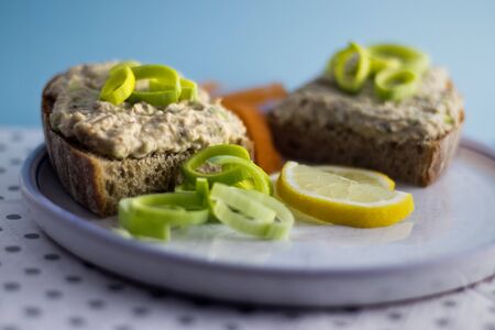 Two slices of bread with fish spread on a plate with green leek and yellow lemonの写真素材
