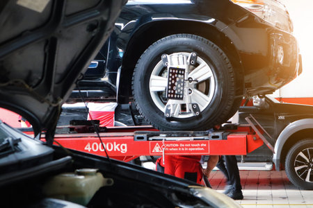 Car mechanic installing sensor during suspension adjustment. Wheel alignment work at repair service stationのeditorial素材