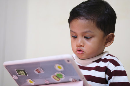 three year old Asian boy at home bed using digital tablet computerの写真素材