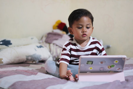 three year old Asian boy at home bed using digital tablet computerの写真素材