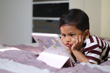 three year old Asian boy at home bed using digital tablet computerの写真素材