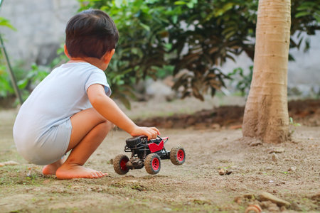 Asian child boy playing car toy on sand outdoor with cute face in nature background. Happy kid enjoy...