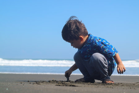 Portrait of little asian baby boy having fun with sand at the beach.