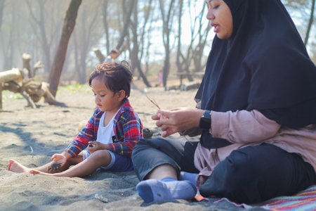 Happy baby boy and mother play sand and toy together on the beach.の写真素材