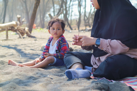 Happy baby boy and mother play sand and toy together on the beach.の写真素材