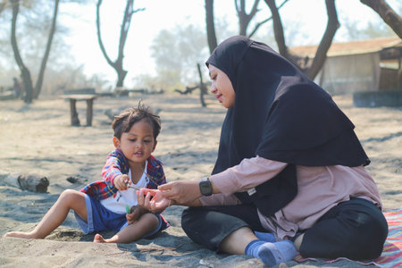 Happy baby boy and mother play sand and toy together on the beach.の写真素材