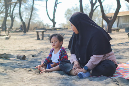 Happy baby boy and mother play sand and toy together on the beach.の写真素材