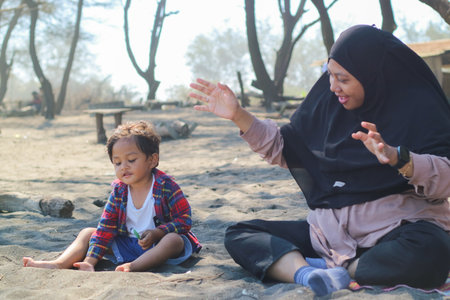 Happy baby boy and mother play sand and toy together on the beach.の写真素材