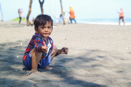 Happy kids have fun in sea surf on black sand beach. Children sit in seashore. Travel lifestyle, swimming activities in family summer camp. Vacations on tropical island.の写真素材
