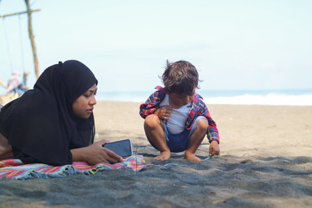 Happy baby boy and muslim mother play sand and toy togather on ther beach.の写真素材