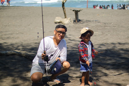 Happy father, fishing and lesson with son on rock with rod by lake, ocean or beach together in nature. Dad with kid, young child or little boy for bonding, teaching or tips to catch by sea waterの写真素材