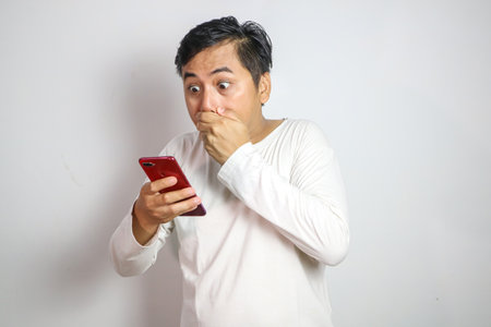Wow face of Asian man covering mouth with hand in white t-shirt get surprised on the smartphone.
