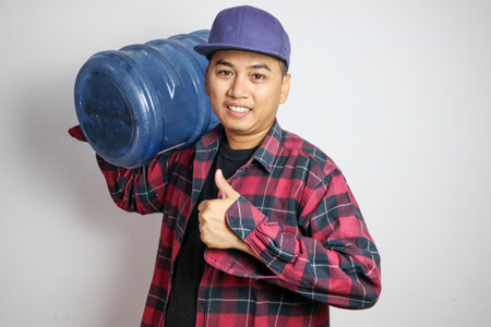 Asian water delivery courier man is holding a bottle on his shoulder. Concept : Drinking water delivery service.の写真素材