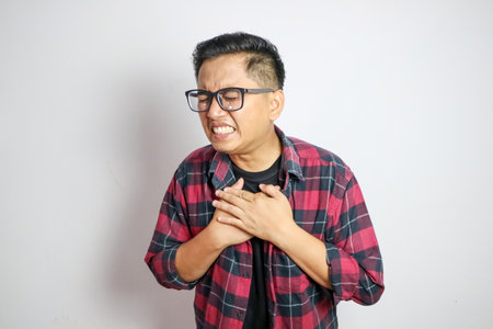 asian man holding hands on chest suffering from heart attack, closeup.