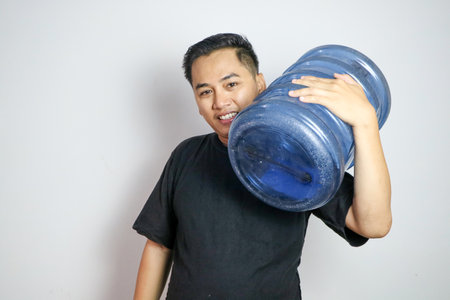 Handsome Asian water delivery courier man is holding a bottle on his shoulder. Concept : Drinking water delivery service.の写真素材
