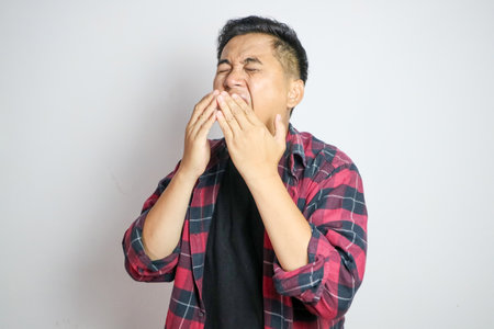A Southeast Asian man sneezing while holding his nose. Captures a moment of discomfort, suitable for themes related to health, allergies, or cold symptoms in various marketing or editorial contextsの写真素材